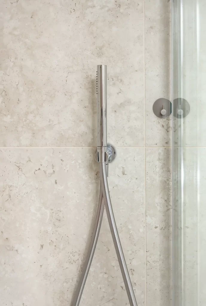 Chrome handheld shower against stone-tiled wall in ensuite