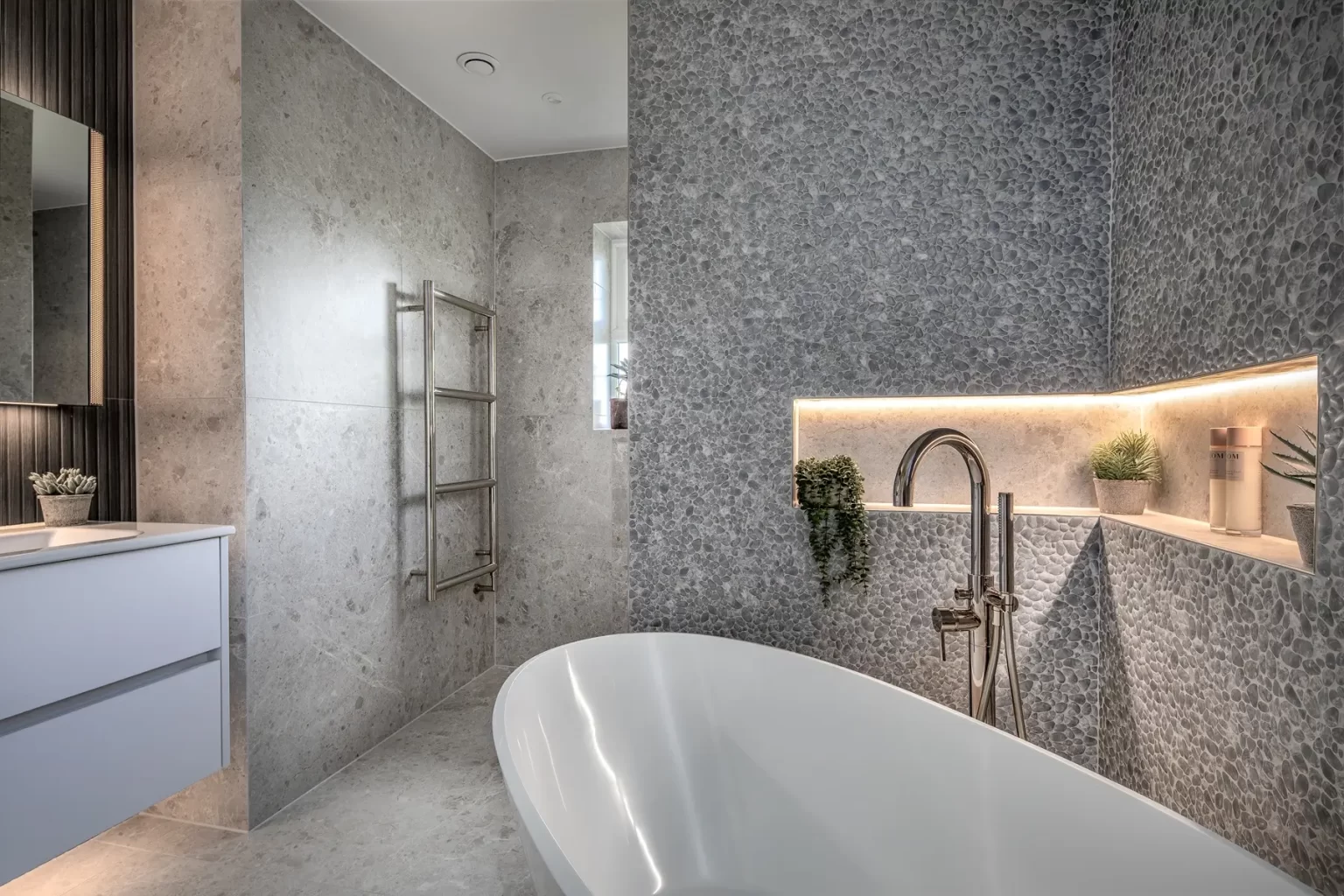Luxury bathroom with freestanding bath, pebble wall, and built-in niche lighting