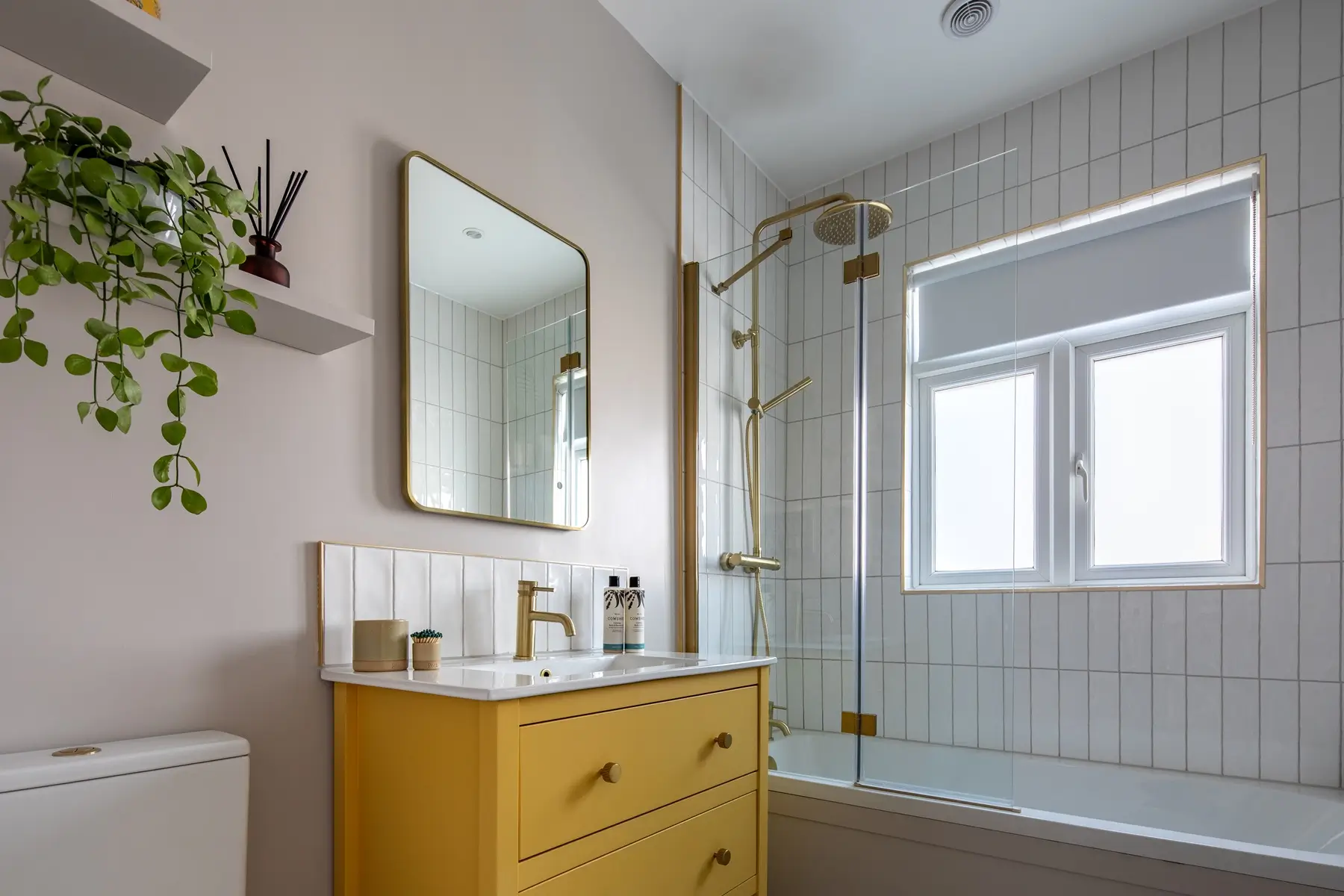 Modern bathroom with yellow vanity unit, brass fixtures, and tiled shower
