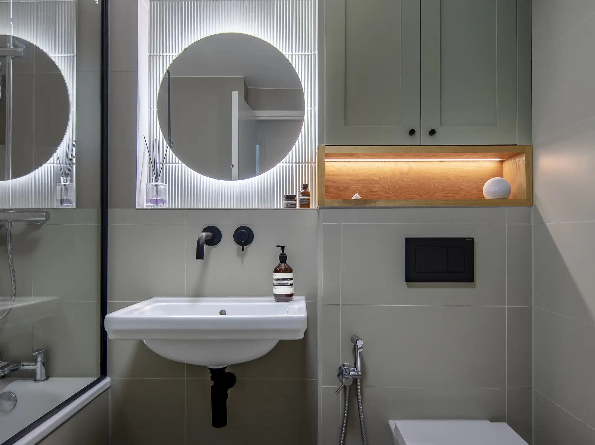 Wall-mounted black basin tap with illuminated fluted mirror and custom cabinetry, part of a South London bathroom renovation.