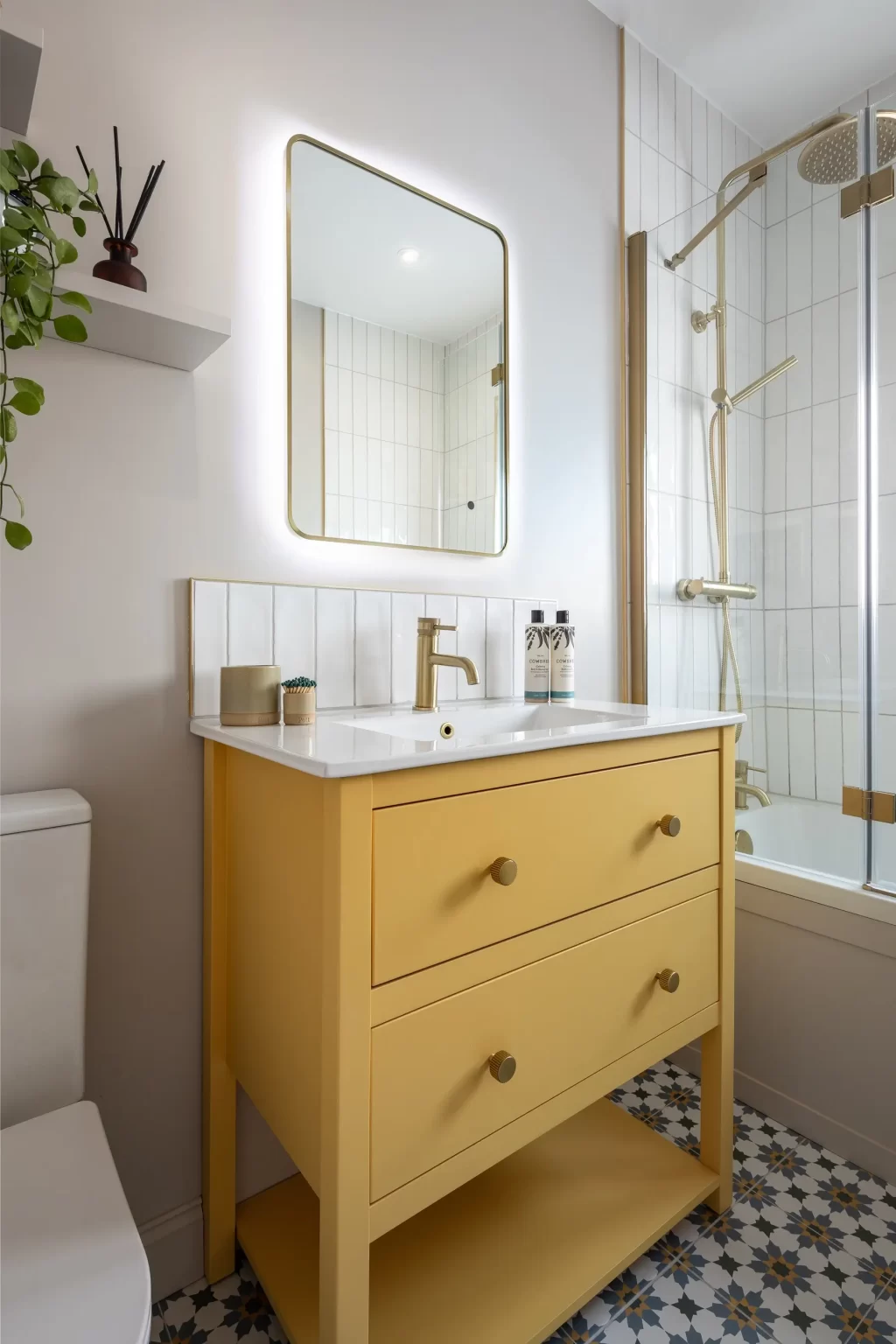 Bathroom with yellow vanity, brass tap, and illuminated mirror