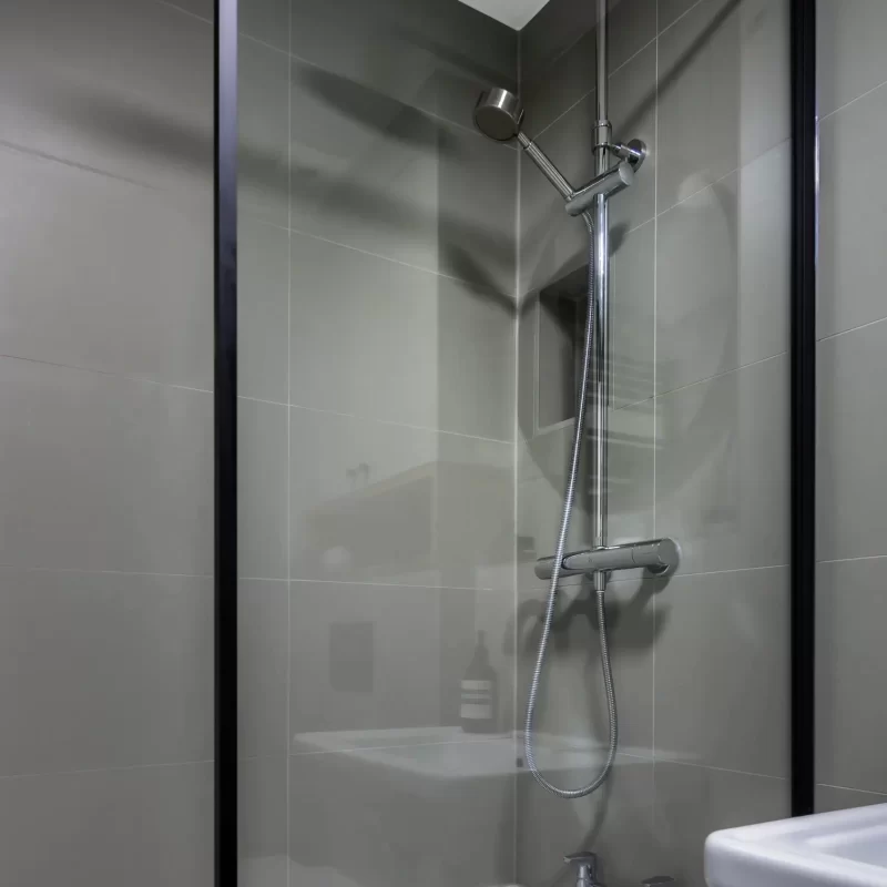Modern bath and shower combination with rainfall shower, handheld spray, and black-framed screen, installed by Surrey bathroom specialists.