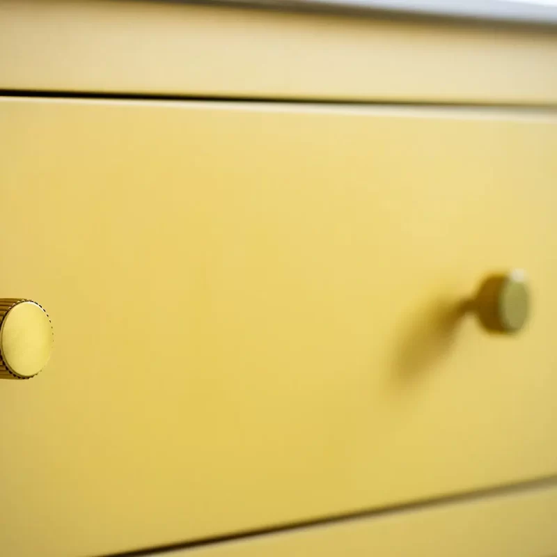 Detail of brass drawer handles on yellow vanity unit
