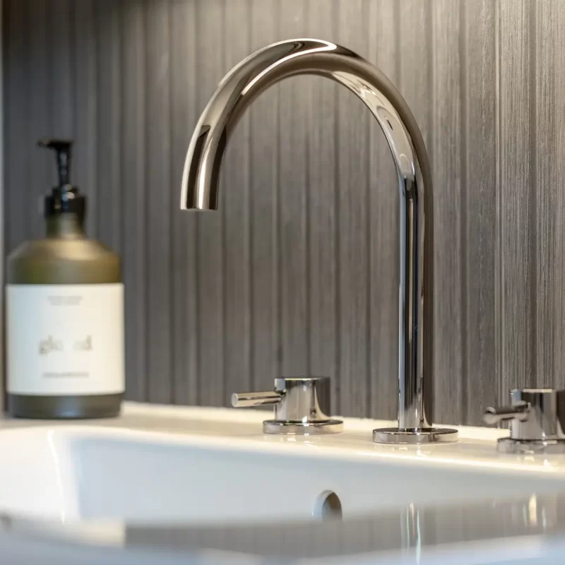 Close-up of chrome basin mixer tap with textured grey backsplash