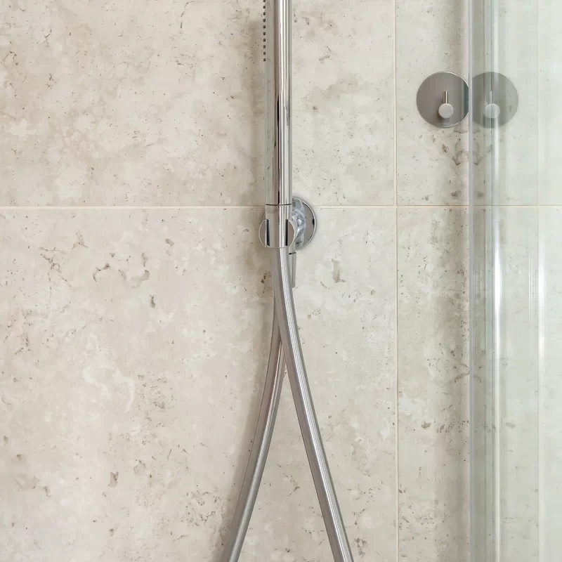 Chrome handheld shower against stone-tiled wall in ensuite
