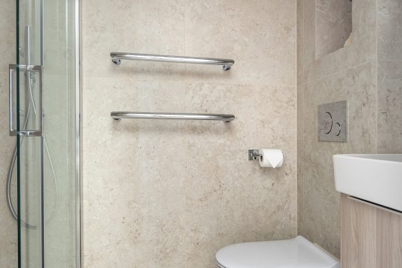 Ensuite bathroom with wall-hung toilet, chrome towel rails, and tiled walls