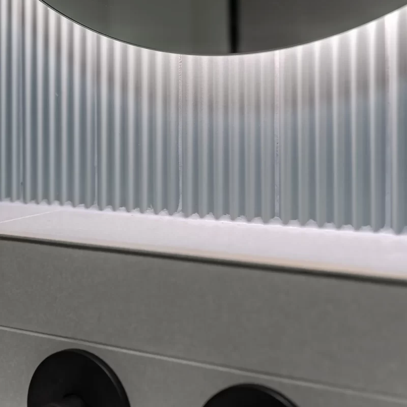 Close-up of fluted bathroom feature tiles with soft backlighting behind the mirror, Kingston upon Thames installation.