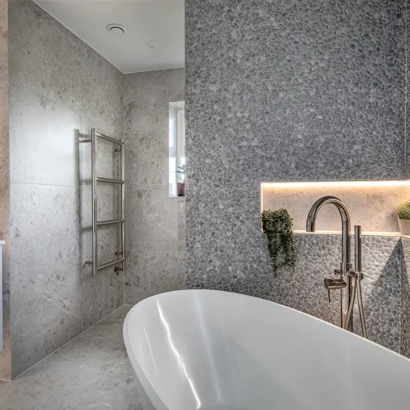 Luxury bathroom with freestanding bath, pebble wall, and built-in niche lighting