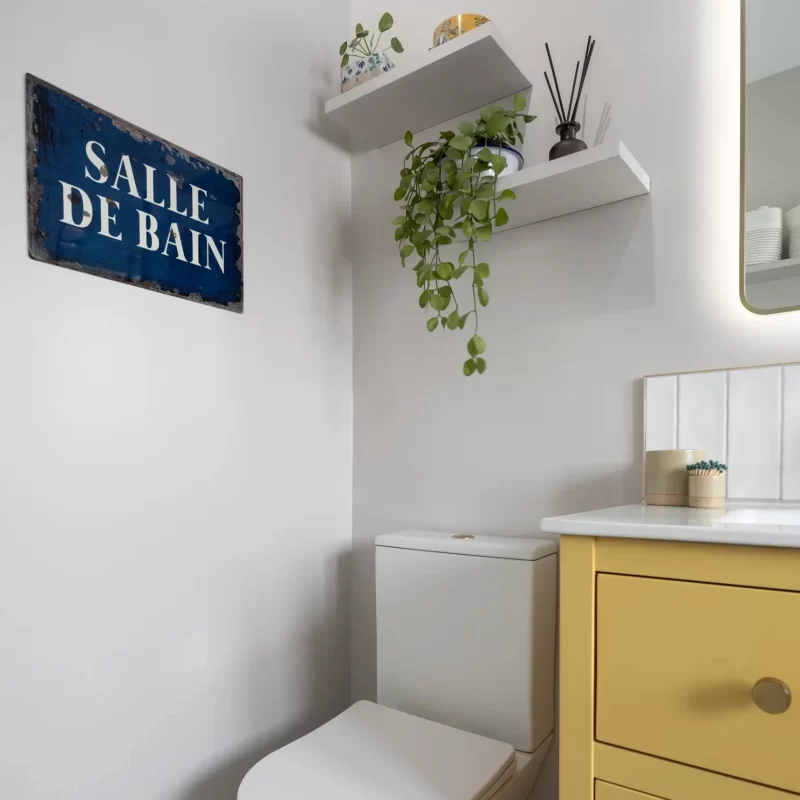 Bathroom corner with toilet, yellow vanity unit, and decorative shelves