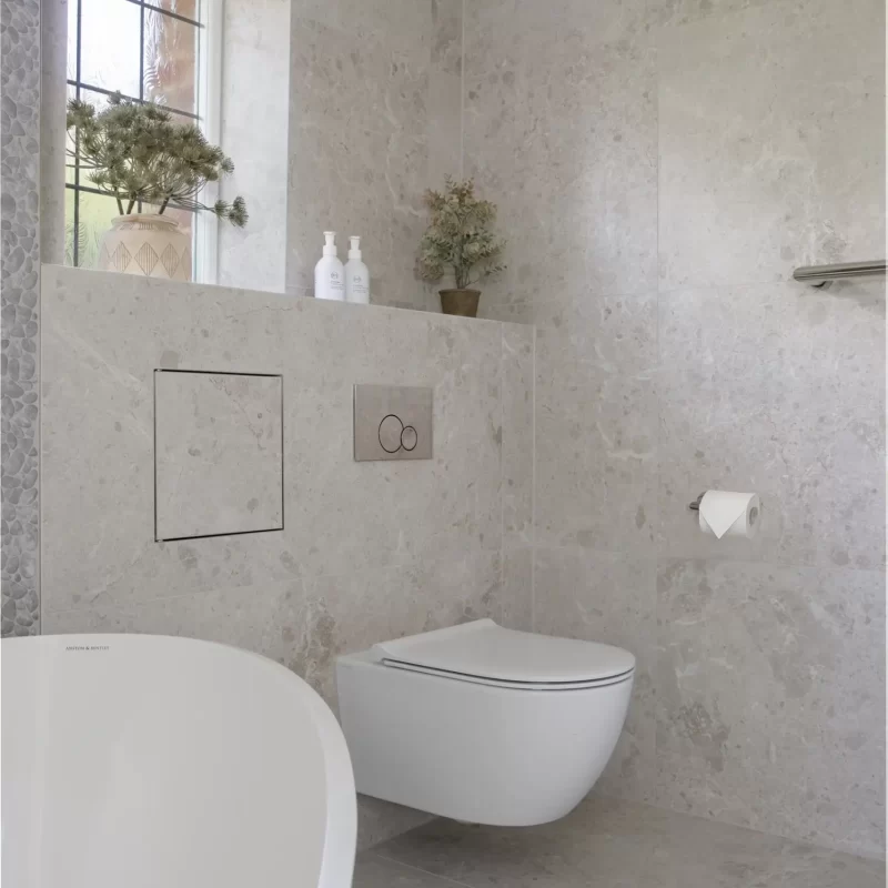 Wall-hung toilet with freestanding bath in stone-tiled bathroom