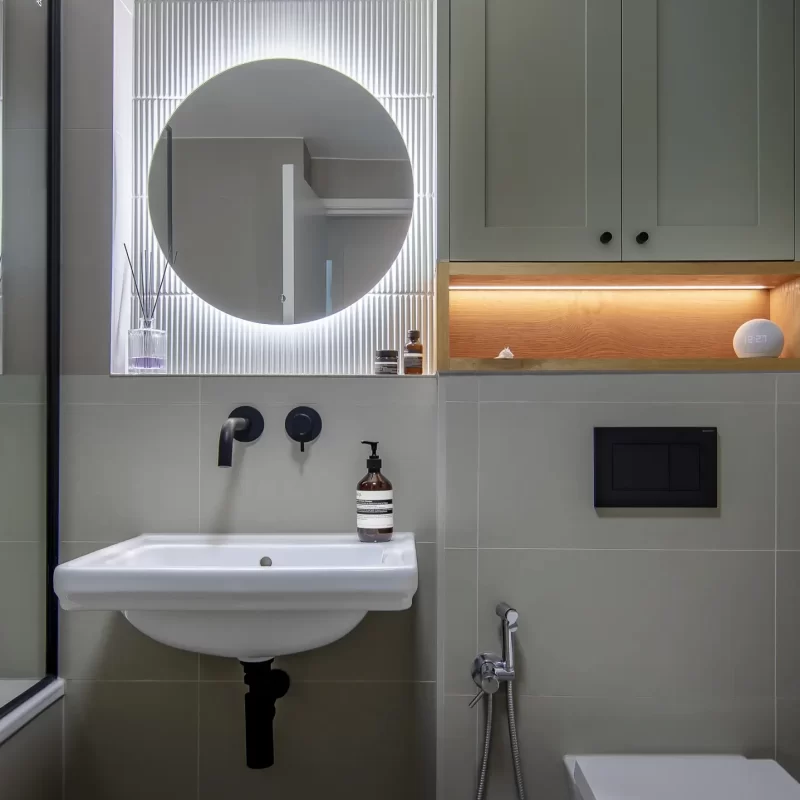 Wall-mounted black basin tap with illuminated fluted mirror and custom cabinetry, part of a South London bathroom renovation.